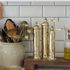 gold kitchen utensils and cooking utensils are on a shelf in front of a white tiled wall