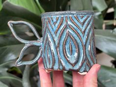 a hand holding a blue and brown ceramic cup with an intricate design on the outside