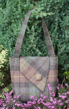 a brown and black plaid purse sitting on top of purple flowers in front of a bush