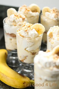 small desserts with bananas and whipped cream in glass cups on a tray next to a banana