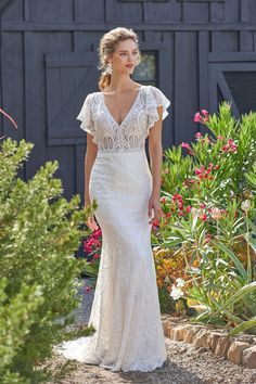 a woman in a white wedding dress walking down a path near some flowers and plants