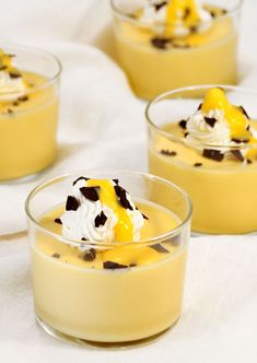 four desserts in small glass bowls with whipped cream and chocolate chips on top, sitting on a white tablecloth