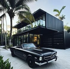 a black car is parked in front of a house with large windows and palm trees