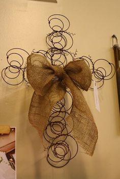 a cross made out of wire and burlock with a bow hanging on the wall