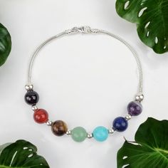 a bracelet with seven chakras on it next to some green leafy leaves