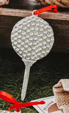 a golf ball shaped glass ornament with red ribbon on the handle and some burlocks around it