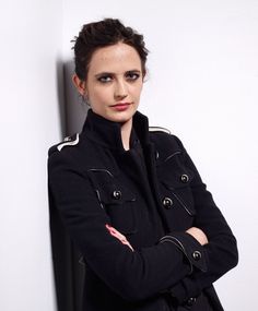 a woman with her arms crossed leaning against a wall wearing a black coat and red lipstick