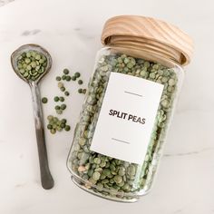 a glass jar filled with green peas next to a spoon on a white counter top