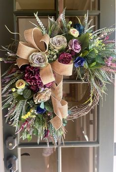 a wreath on the front door with flowers and greenery hanging from it's side