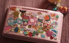 a pink suitcase with many stickers on the lid and some stuffed animals sitting next to it