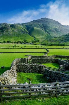 an old stone wall in the middle of a green field with mountains in the background