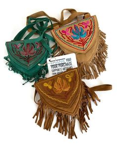 three bags with fringes and designs on them, one has a name tag attached to it