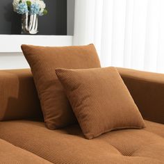 two brown pillows sitting on top of a couch next to a vase with flowers in it