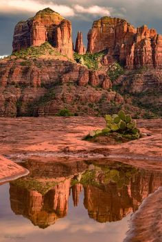 the red rocks are reflected in the still water at the base of the mountain range