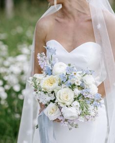 a woman in a wedding dress holding a bouquet of white and blue flowers on her shoulder