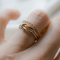 a woman's hand wearing a gold ring with twisted design on the middle finger