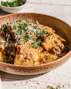 a brown bowl filled with pasta and meat covered in parmesan cheese on top of a table