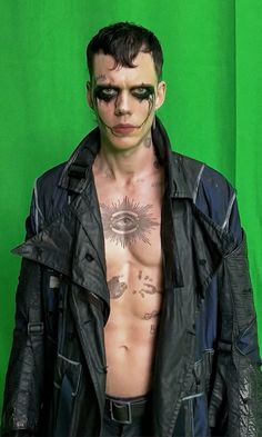 a shirtless man with his face painted like an eyeball is standing in front of a green background