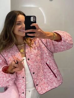 a woman taking a selfie in front of a mirror wearing a pink jacket and white pants