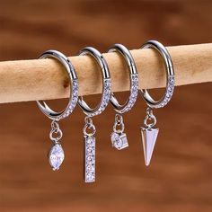 three pairs of hoop earrings hanging from a wooden stick with clear crystal stones and an arrow charm