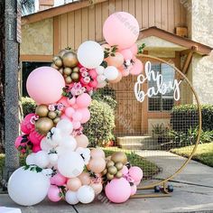 a pink and gold balloon arch on the side of a house for a baby shower