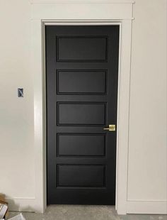 an empty room with a black door and some boxes on the floor next to it