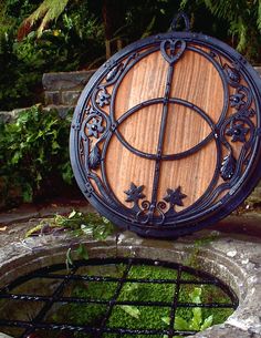 a circular wooden sign sitting on top of a stone wall next to a green plant