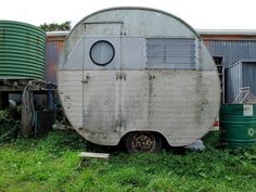 an old trailer sitting in the grass next to some metal tanks and water tank containers