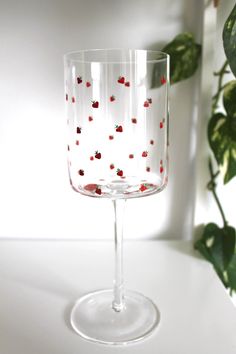 a wine glass with red berries on the bottom and white dots in the middle, sitting next to a potted plant