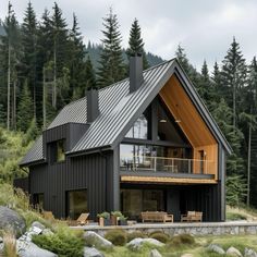 a black house with a wooden deck in the middle of some trees and rocks on the ground