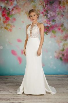 a woman standing in front of a floral backdrop wearing a white dress with sheer neckline