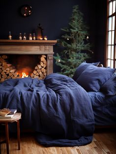 a bed with blue sheets and pillows next to a fire place in front of a christmas tree