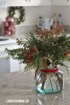 a glass jar filled with red berries and greenery on top of a kitchen counter