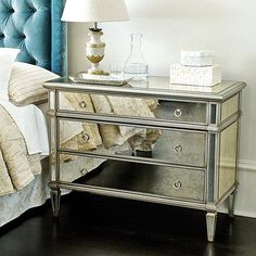 a bedroom with a mirrored dresser next to a blue headboard and white bedding