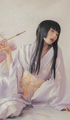 a woman in a kimono holding a paintbrush and looking at the camera while sitting down