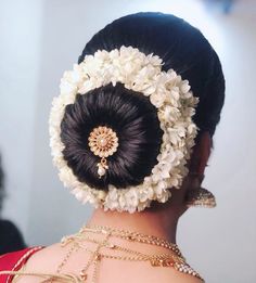 the back of a woman's head with white flowers in her hair and gold jewelry