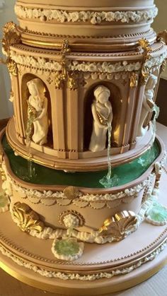 a three tiered cake decorated with figurines and gold trimmings on a table