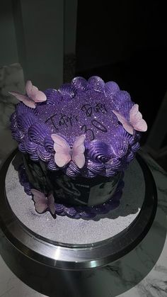 a purple cake with butterflies on it sitting on top of a marble table next to a mirror