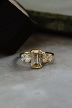 an emerald cut diamond ring with three smaller diamonds on it's side, set in yellow gold and white gold