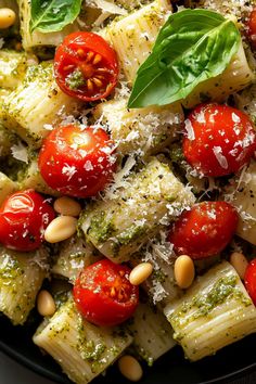 pasta with pesto, tomatoes, pine nuts and parmesan cheese in a black bowl