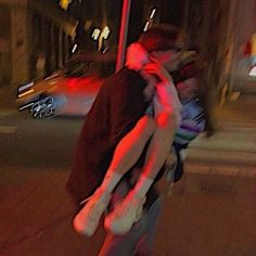 two people hugging each other on the street at night with traffic lights in the background