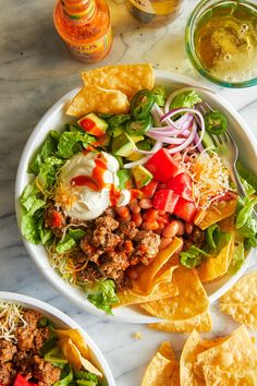 two plates filled with taco salad and tortilla chips on a marble table