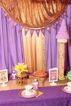 a purple table topped with plates and cups next to a gold drape covered wall