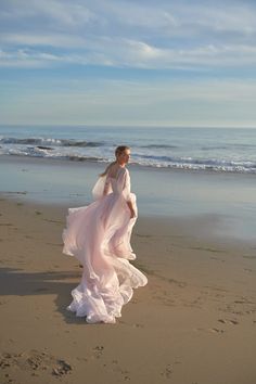 a woman in a white dress is walking on the beach