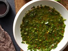 a white bowl filled with green sauce on top of a wooden cutting board