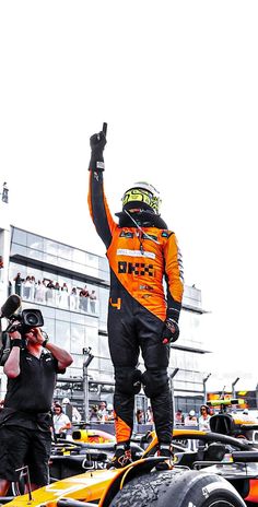 a man standing on top of a race car with his hand up in the air