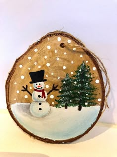 a wooden slice with a snowman and tree on it's side in the snow