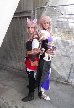 two people dressed in cosplay costumes standing next to each other near a fence