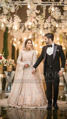 a man and woman dressed in formal wear standing next to each other with chandeliers hanging from the ceiling