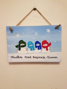 a sign hanging on the side of a wall with three snowmen wearing hats and scarfs